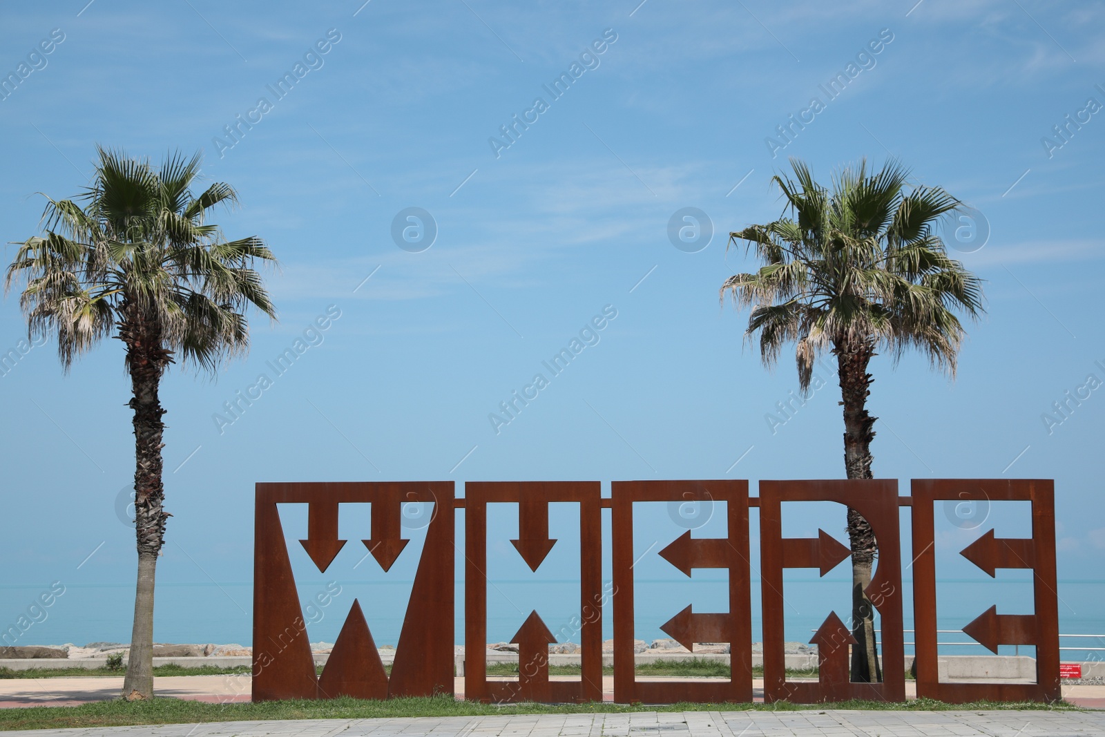 Photo of BATUMI, GEORGIA - JUNE 10, 2022: Beautiful art installation with word WHERE and palm trees near sea on sunny day