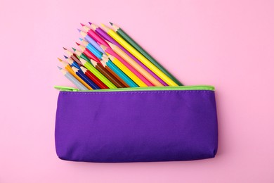 Many colorful pencils in pencil case on pink background, top view