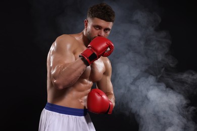 Photo of Man wearing boxing gloves in smoke on black background. Space for text