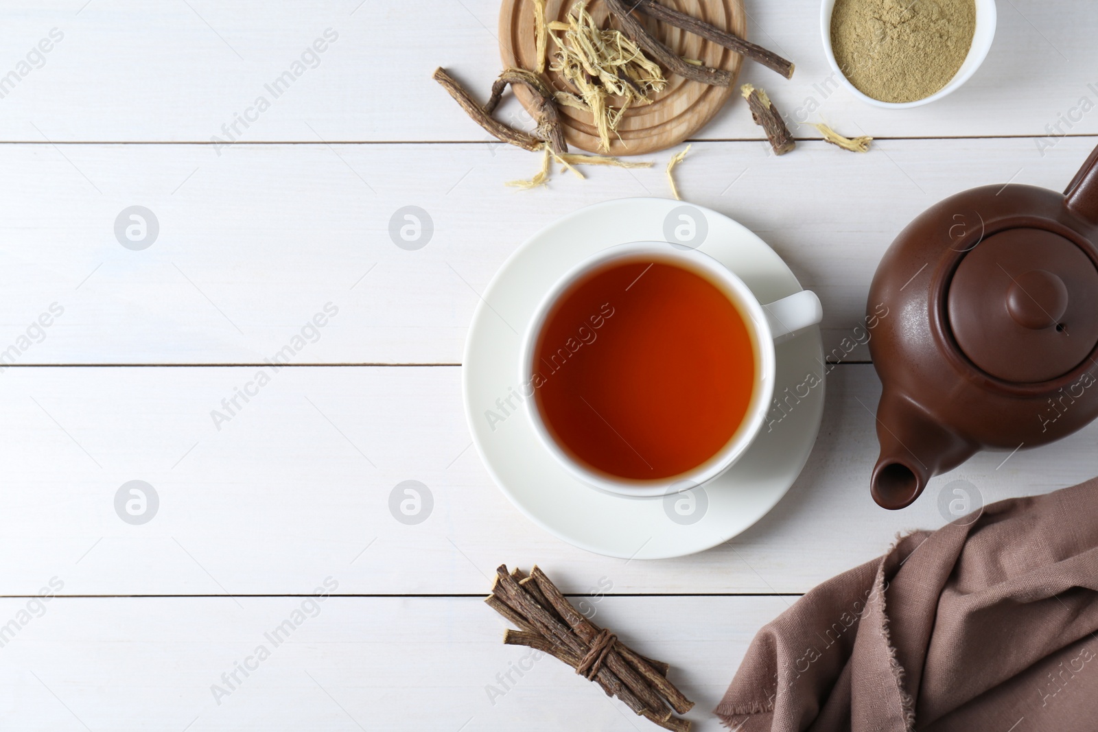 Photo of Aromatic licorice tea in cup, dried sticks of licorice root and powder on white wooden table, flat lay. Space for text