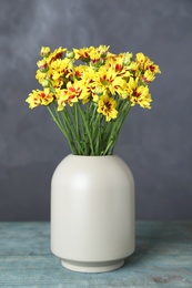 Photo of Vase with beautiful chrysanthemum flowers on light blue wooden table against grey background