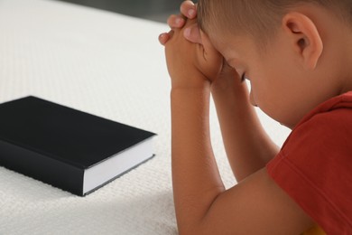 Cute little boy with hands clasped together saying bedtime prayer over Bible at home, closeup