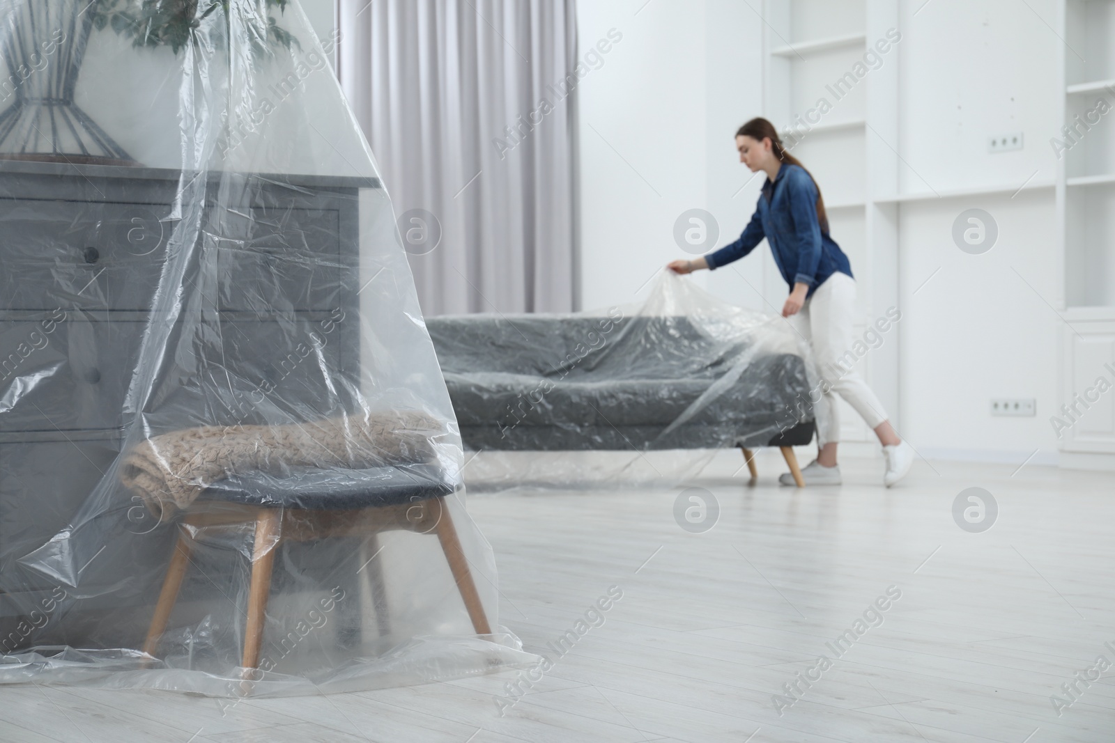 Photo of Young woman putting plastic film away from sofa at home, selective focus