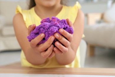 Photo of Little girl playing with bright kinetic sand at table indoors, closeup