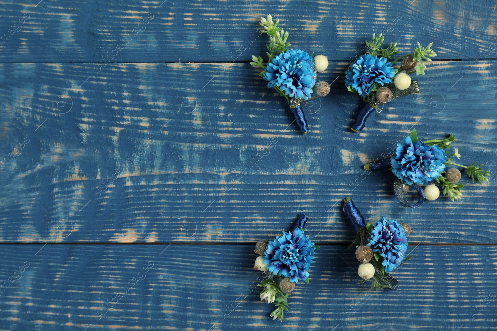 Photo of Stylish boutonnieres on blue wooden table, flat lay. Space for text