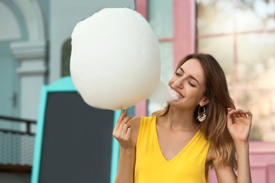 Photo of Happy young woman eating cotton candy outdoors