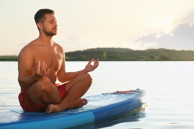 Photo of Man meditating on light blue SUP board on river at sunset