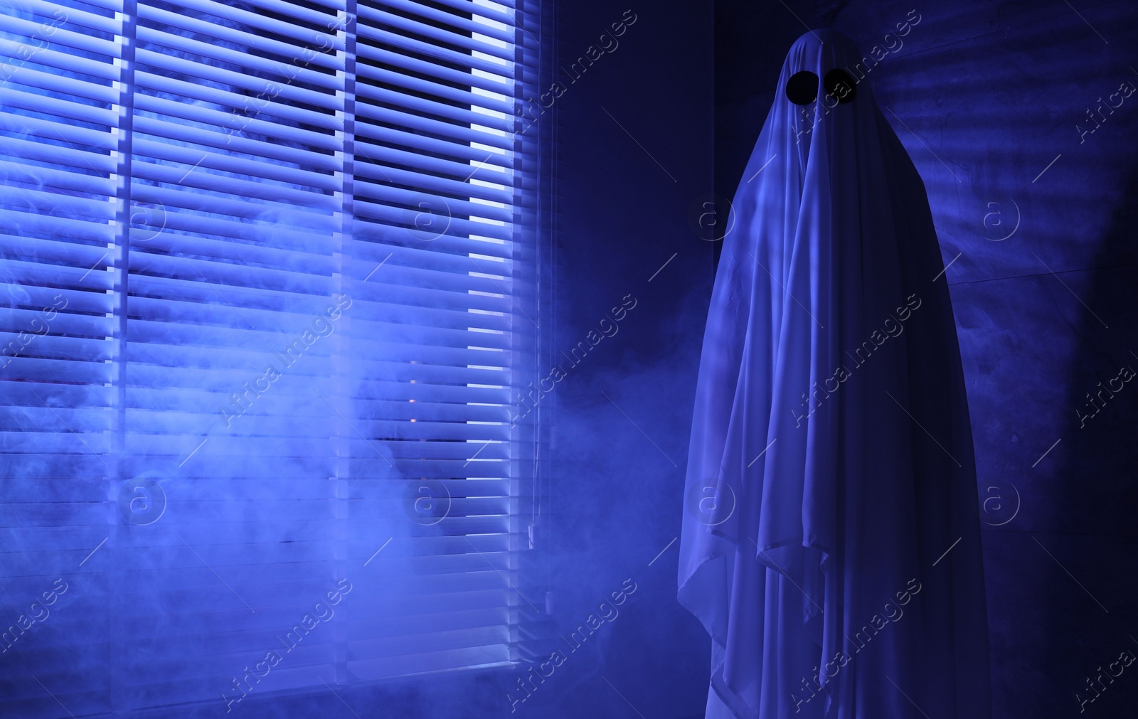 Photo of Creepy ghost. Woman covered with sheet near window in blue light