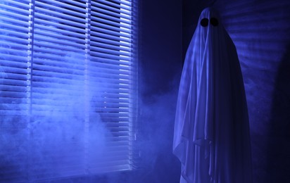 Photo of Creepy ghost. Woman covered with sheet near window in blue light