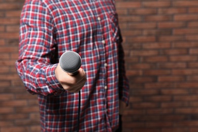 Young man in shirt holding microphone near brick wall, closeup with space for text