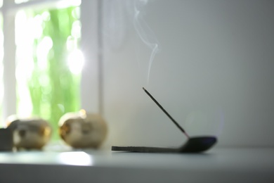 Photo of Incense stick smoldering on table in room. Space for text