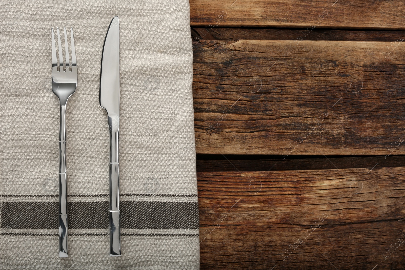 Photo of Fork, knife and napkin on wooden table, top view with space for text. Stylish shiny cutlery set