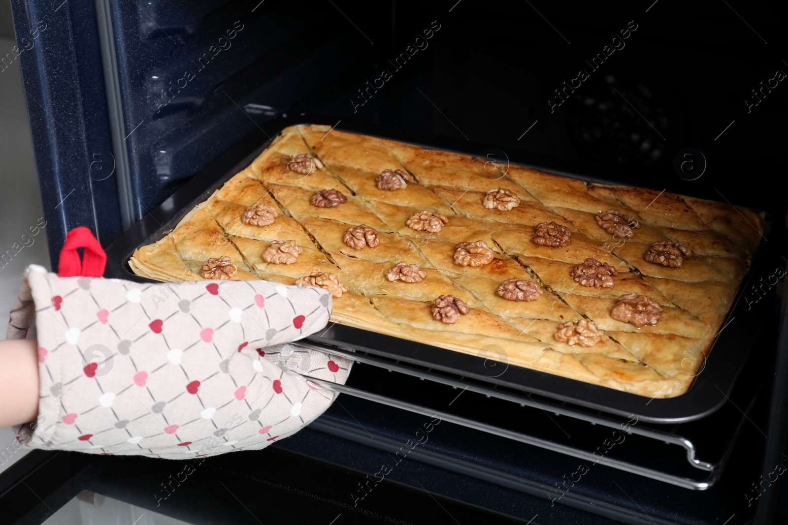 Photo of Woman taking out baking pan with delicious baklava from oven, closeup