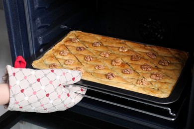 Woman taking out baking pan with delicious baklava from oven, closeup