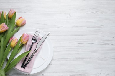 Photo of Stylish table setting with cutlery and tulips on white wooden background, flat lay. Space for text
