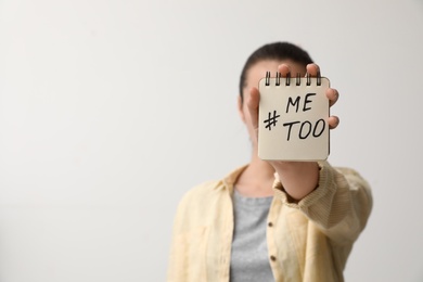 Woman holding notebook with hashtag MeToo against light background, closeup. Stop sexual assault