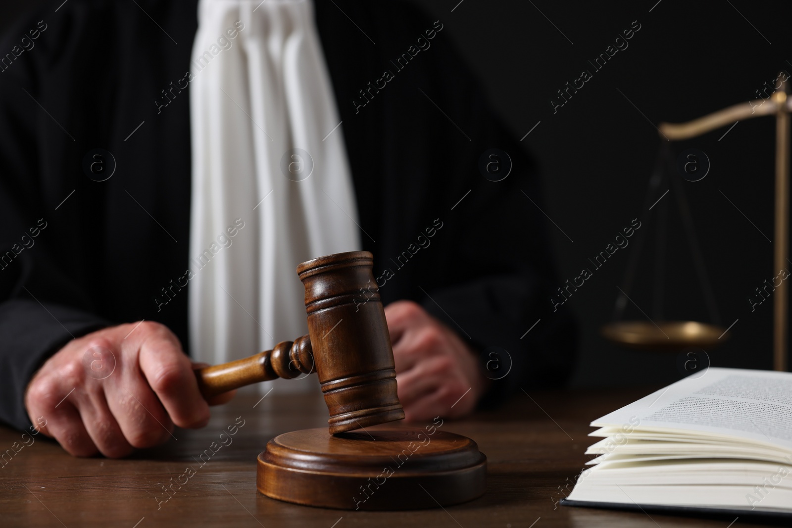 Photo of Judge with gavel sitting at wooden table against black background, closeup