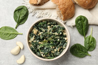 Photo of Tasty spinach dip with egg in bowl, bread and garlic on grey table, flat lay