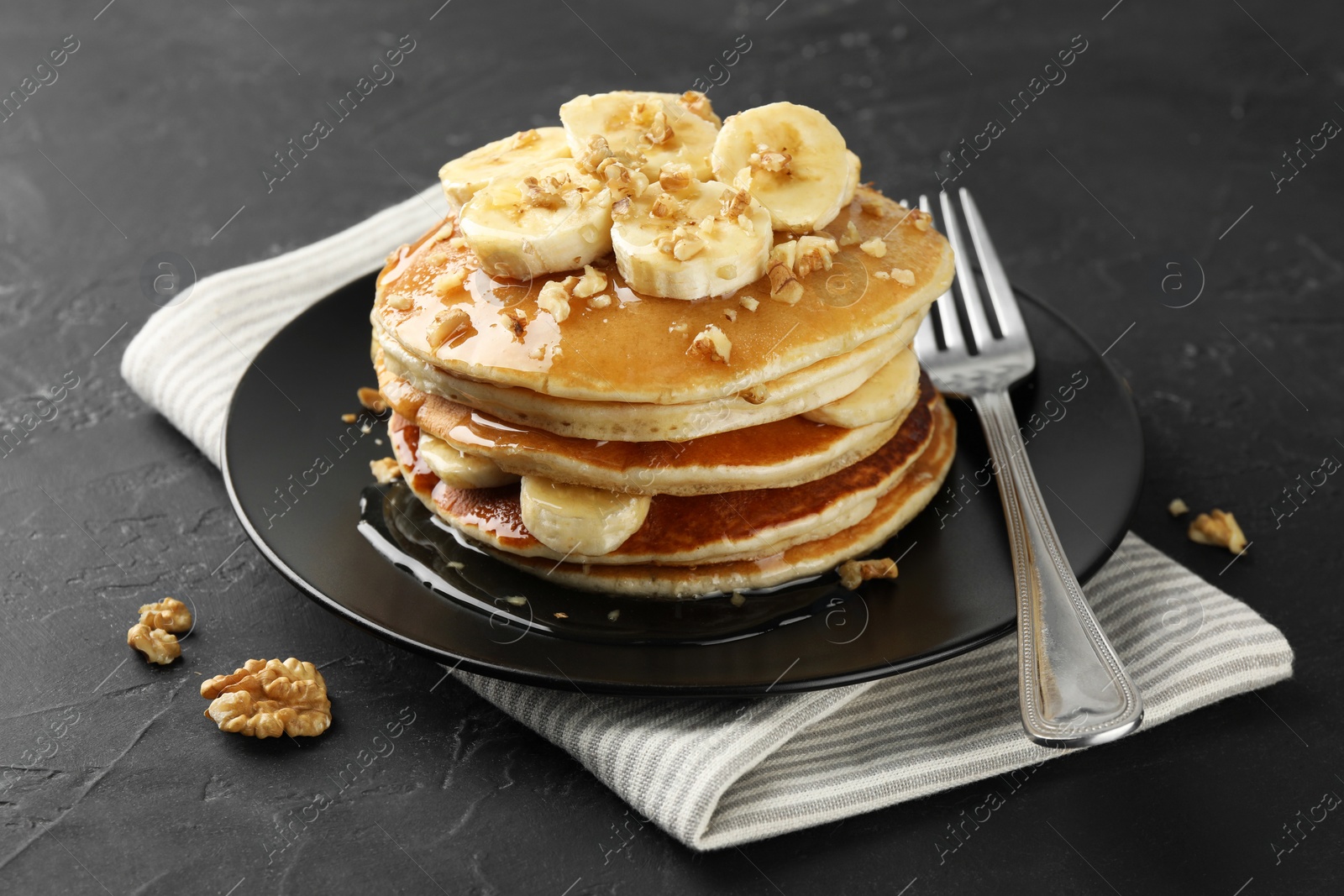 Photo of Delicious pancakes with bananas, walnuts and honey on dark textured table, closeup