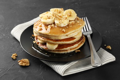 Photo of Delicious pancakes with bananas, walnuts and honey on dark textured table, closeup