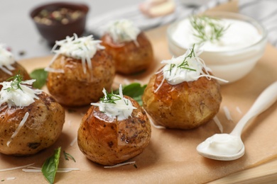 Photo of Delicious baked potato with sour cream on wooden board, closeup