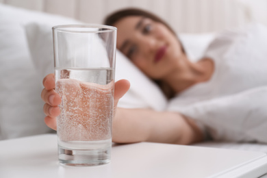 Photo of Young woman taking glass of water from nightstand at home, closeup