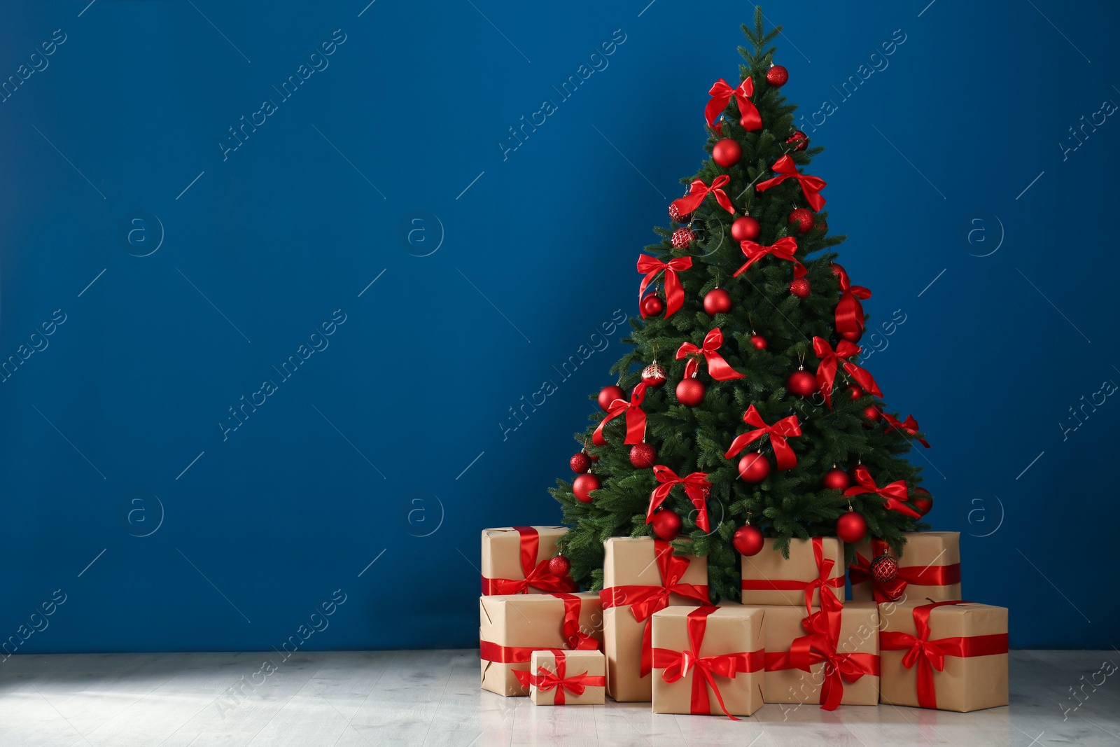 Photo of Decorated Christmas tree and gift boxes near blue wall. Space for text