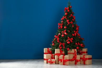 Photo of Decorated Christmas tree and gift boxes near blue wall. Space for text