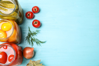 Photo of Glass jars with different pickled vegetables on light blue wooden table, flat lay. Space for text