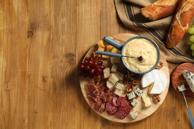 Photo of Fondue pot with tasty melted cheese, forks and different snacks on wooden table, top view. Space for text