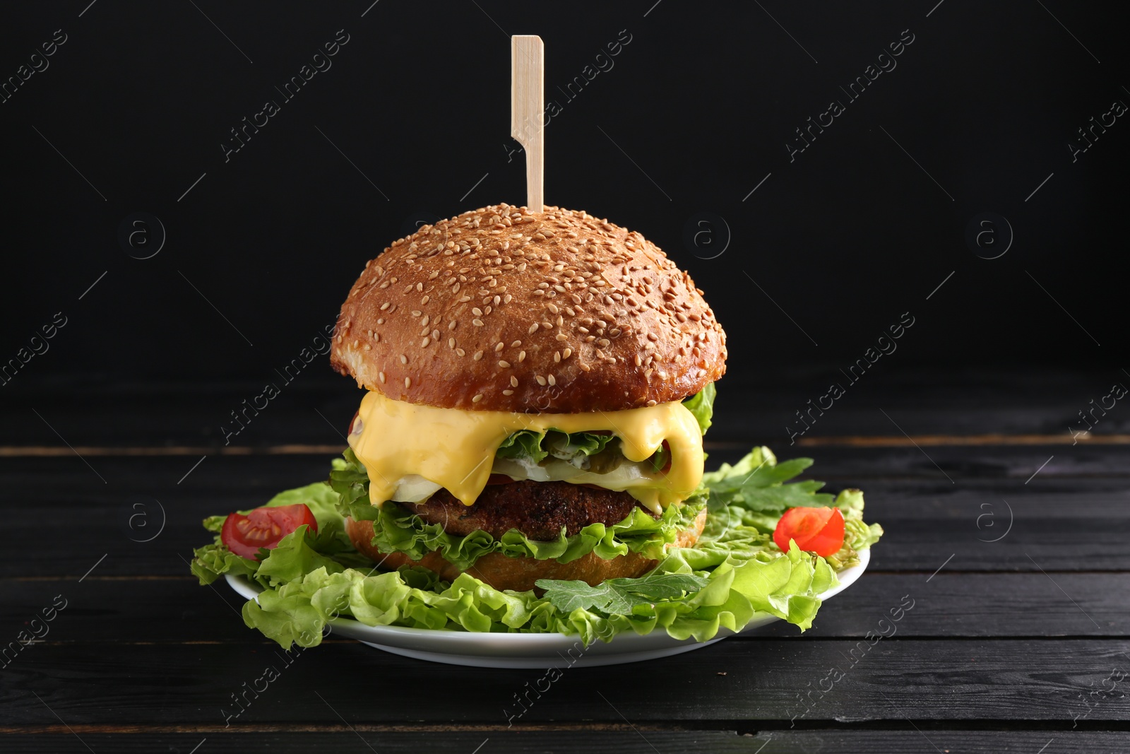 Photo of Vegetarian burger with delicious patty and cheese on black wooden table