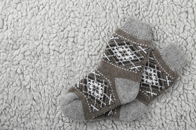Photo of Knitted socks on grey fur background, flat lay. Space for text