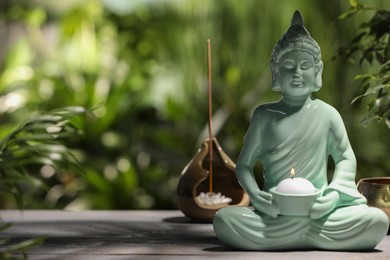Buddhism religion. Decorative Buddha statue with burning candle on wooden table outdoors, space for text