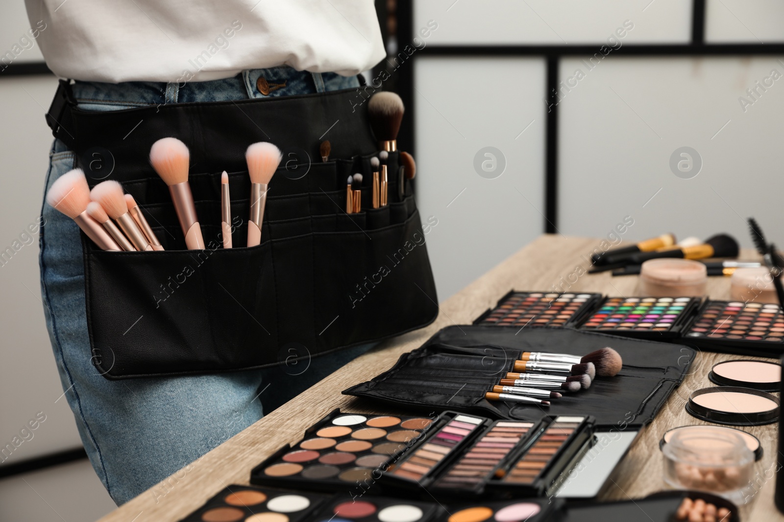 Photo of Professional makeup artist with belt organizer near wooden table indoors, closeup