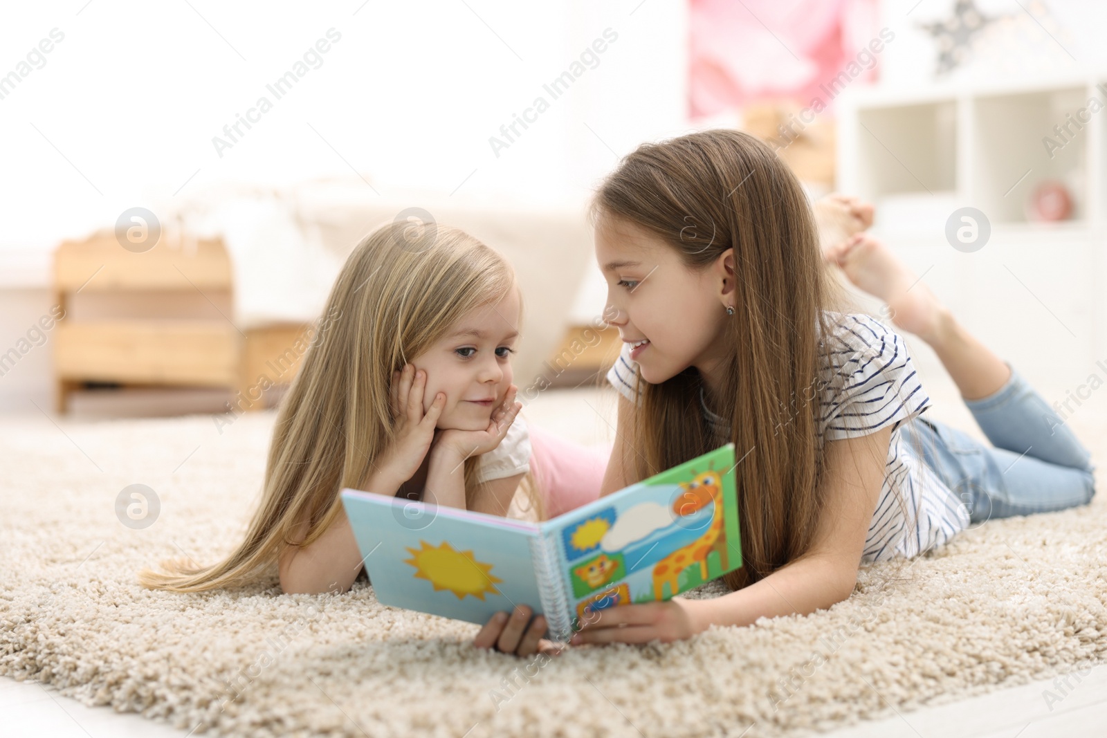 Photo of Cute little sisters reading book together at home