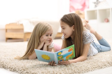 Cute little sisters reading book together at home