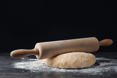 Photo of Raw wheat dough with flour and rolling pin on table