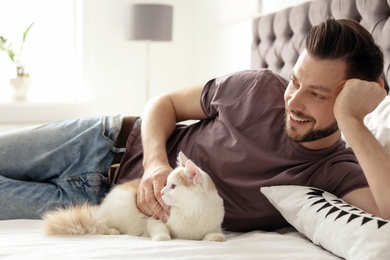 Photo of Young man with cute cat on bed at home