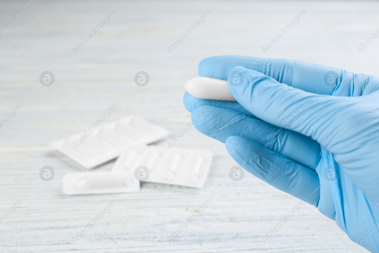 Photo of Woman holding suppository at white wooden table, closeup. Hemorrhoid treatment