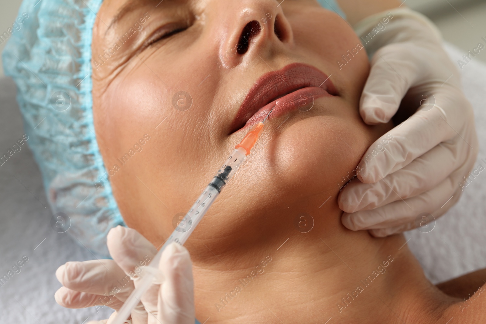 Photo of Doctor giving lips injection to senior woman in clinic, closeup. Cosmetic surgery