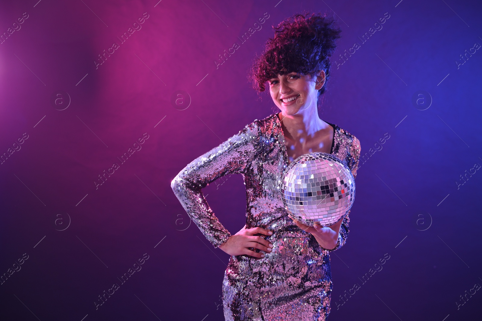 Photo of Beautiful young woman with disco ball posing on color background in neon lights. Space for text