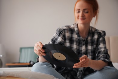Young woman with vinyl disc for turntable in bedroom