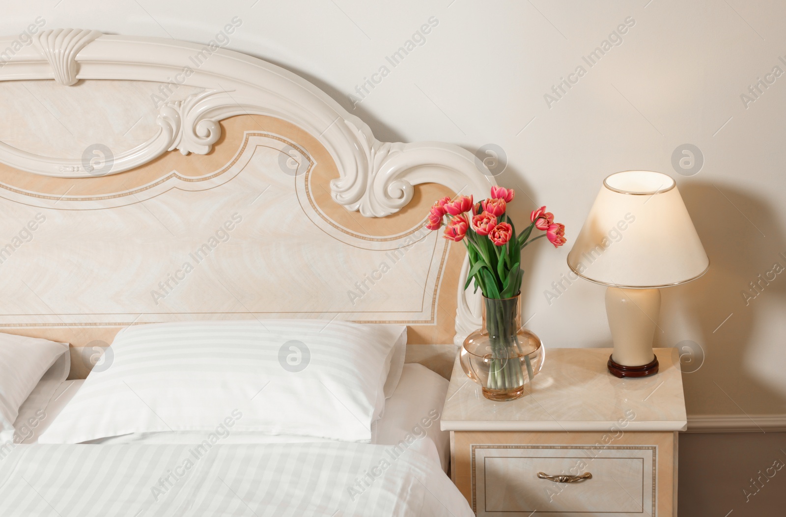 Photo of Stylish bedroom interior with comfortable bed, lamp and vase of flowers