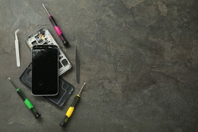 Parts of damaged smartphone and repair tool set on grey table, flat lay. Space for text
