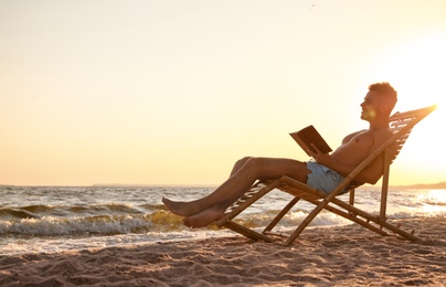 Photo of Young man reading book in deck chair on beach