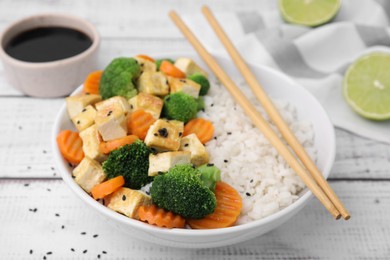 Bowl of rice with fried tofu, broccoli and carrots on white wooden table, closeup