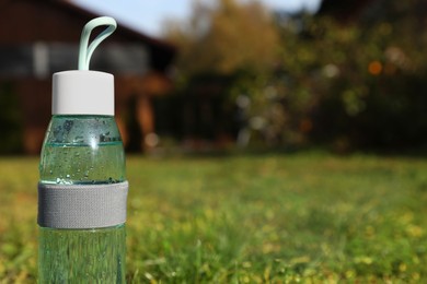 Glass bottle of fresh water on green grass outdoors. Space for text
