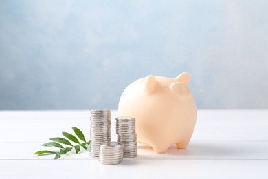 Financial savings. Piggy bank, stacked coins and green twig on white wooden table