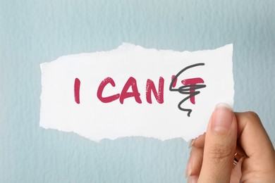 Image of Woman holding note with phrase I CAN'T with crossed out letter T on light background, closeup. Motivation and positivity