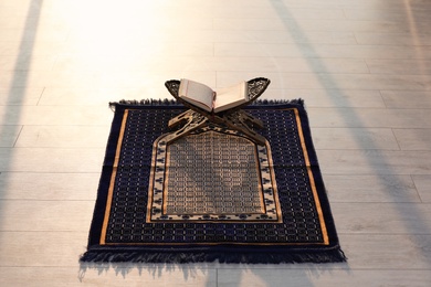 Photo of Rehal with open Quran on Muslim prayer mat indoors